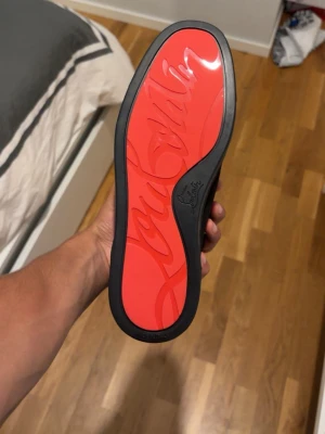 Svarta sneakers från Christian Louboutin - Stilrena svarta sneakers från Christian Louboutin i mocka med svarta skosnören och diskret design. Låg modell med beige innerfoder och klassisk röd Louboutin-logga på tillbehör. Perfekta för dig som gillar exklusiva och minimalistiska skor.
