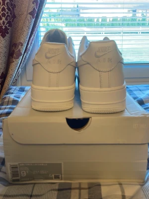 Nike Air Force 1 vita sneakers - Klassiska Nike Air Force 1 sneakers i helvitt läder med perforerad tåbox och vita skosnören. Snygg och tidlös modell med Nike-logga på hälen och tungan. Passar perfekt till streetwear och har en chunky sula för extra stilpoäng.