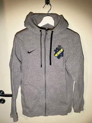 Grå AIK hoodie från Nike - Säljer en grå hoodie från Nike med AIK-emblem på bröstet i storlek S. Hoodien har dragkedja framtill, två fickor och justerbar huva med svarta snören. Perfekt för dig som vill representera AIK med stil.