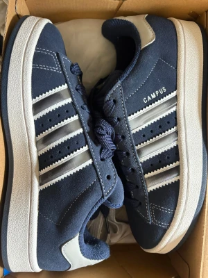 Adidas Campus 00s blå sneakers - Helt osnvända mörkblå Adidas Campus sneakers i mocka med vita detaljer och klassiska tre ränder på sidorna. Skon har vit sula, blå skosnören och CAMPUS-tryck på sidan. 