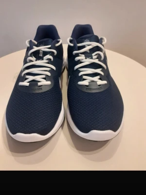 Marinblå Nike sneakers med vit sula - Snygga marinblå sneakers från Nike med vit sula och vita skosnören. Ovandelen är i meshmaterial för bra andningsförmåga och skon har en låg profil. Klassisk Nike-logga på sidan i vitt och bekväm, vadderad insida.