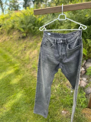 Grå raka jeans med hög midja - Säljer ett par grå jeans med rak passform och hög midja. Jeansen har klassiska fem fickor, bälteshällor och knappgylf. Materialet är denim i bomull och färgen har en snygg tvättad look. Perfekta för en avslappnad och trendig stil.