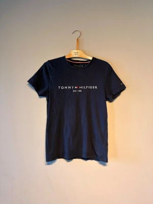 Marinblå t-shirt från Tommy Hilfiger - Snygg marinblå t-shirt från Tommy Hilfiger med tryckt logga och text 'EST. 1985' på bröstet. Klassisk rund halsringning och korta ärmar. Perfekt basplagg i mjuk bomull som funkar till allt.