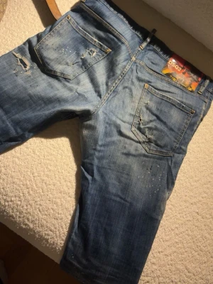 Ljusblå slitna jeans med hål - Säljer ett par ljusblå jeans med slitningar och hål på både fram- och baksida. Jeansen har fem fickor, raka ben och coola detaljer som ger en trendig, avslappnad look. Perfekta för dig som gillar streetstyle och en lite ruffare stil.