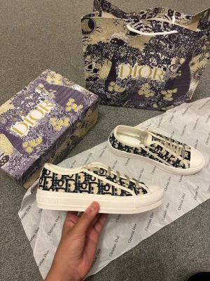Dior Oblique låga sneakers - Snygga låga sneakers från Dior med klassiskt blått och vitt Oblique-mönster. Skorna har vita snören, vit sula och detaljer med 'Christian Dior' på sidan och tungan. Tillverkade i canvasmaterial för en trendig och exklusiv look.