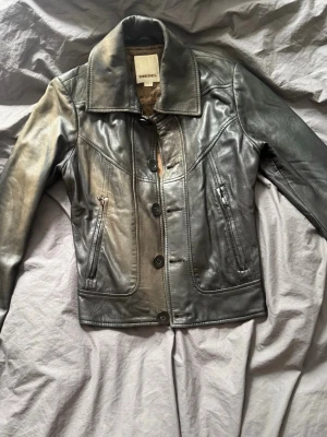 Svart skinnjacka från Diesel - Snygg svart skinnjacka från Diesel i äkta skinn. Snygga sömdetaljer och coolt mönstrat innerfoder. Perfekt för dig som vill ha en tidlös och edgy look. Jackan har missfärgningar som ni kan se på bilden 