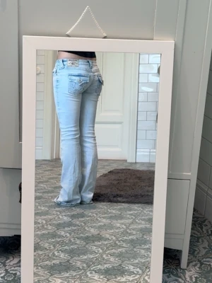 Ljusblå bootcut jeans med låg midja - Säljer ett par ljusblå bootcut jeans med låg midja och snygga detaljer på bakfickorna. Jeansen har klassisk femficksdesign och är tillverkade i denim med lite stretch för skön passform. Perfekta för dig som gillar en retro vibe och vill ha ett par jeans som sticker ut. Dom är lite trasiga nere vid fötterna, kan skicka dom samma dag eller dagen efter att köpet gått igenom 