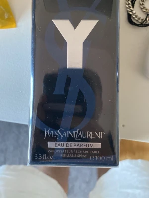 Yves Saint Laurent Y Eau de Parfum - Y Eau de Parfum från Yves Saint Laurent är en elegant parfym i en mörkblå och svart rektangulär flaska med silverdetaljer. Flaskan rymmer 100 ml och har en modern, stilren design med tydlig Y-logga på framsidan.