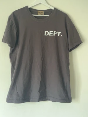 Brun t-shirt från Gallery Dept. - Cool brun t-shirt från Gallery Dept. med trycket 'DEPT.' på bröstet och större tryck på ryggen med adress och logga. Klassisk passform och rund hals. Perfekt för dig som gillar streetwear och vill sticka ut med en unik look.