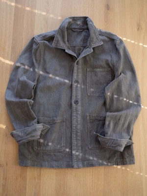 Brun Chore Jacket, size S - Snygg grå overshirt i bomull med tre stora utanpåliggande fickor och knäppning framtill. Klassisk krage och avslappnad passform, perfekt att slänga över en t-shirt. Ärmarna kan vikas upp för en mer casual look.
