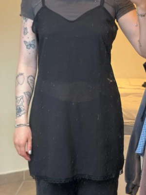 Svart nattlinne med spetsdetaljer - Gullig svart mini klänning. Lite genomskinligt tyg och med spets längst ner. Storlek 42.  köpt secondhand. Använd av mig ca 3 gånger.
