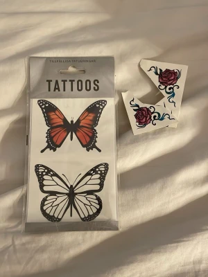 Tillfälliga tatueringar fjäril & ros - Säljer ett set med tillfälliga tatueringar som innehåller två fjärilar i svartvitt och orange samt två rosor med blå detaljer. Perfekt för maskerad eller cosplay när du vill ha en cool och kreativ look.