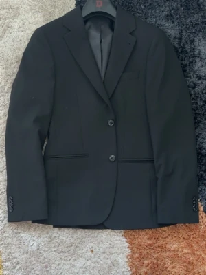 Svart klassisk kostym  - En stilren svart kostym som passar perfekt till bal eller stundet eller andra tillfällen som bröllop. Jag har själv använt den bara 1 gång. Kavajen är i storlek 44R och byxorna är i storlek 29-30. Passar perfekt till dig som köper storlek S på kläder. Kontakta mig vid intresse och pris kan diskuteras. 