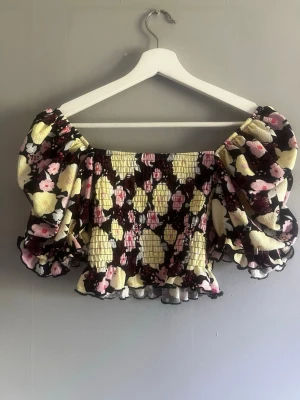 Bik Bok Blommig croppad topp med puffärm - Söt croppad topp med blommigt mönster i svart, gul och rosa. Toppen har stora puffärmar och smockad midja för en trendig look. Perfekt för dig som vill sticka ut med färg och volym.