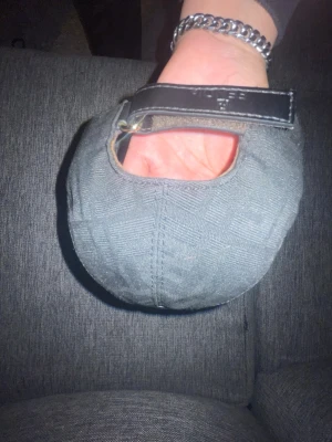 Svart keps från Fendi med läderdetalj - Snygg svart keps från Fendi med justerbart spänne i läder och guldfärgad metallring. Kepsen är tillverkad i bomull och har diskret mönster i tyget. Insidan är fodrad i brunt tyg för extra komfort. Perfekt accessoar för en trendig streetwear-look.