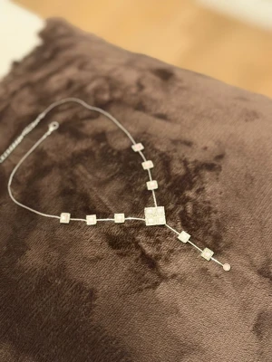 Silvrigt halsband med fyrkantiga detaljer - Snyggt halsband i silverfärg med flera fyrkantiga hängen i olika storlekar. Hängena har små glittrande stenar som ger ett elegant intryck. Kedjan är tunn och halsbandet har en modern, geometrisk design som sticker ut.
