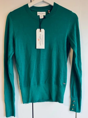 Ny stickad tröja Holly & Whyte. XS. NWT.  - Ny snygg finstickad tröja från Holly & Whyte med rund halsringning och långa ärmar. Tröjan har ribbade muddar och dekorativa knappar vid ärmsluten. Storlek XS. Perfekt till jeans eller kjol för en stilren look. Oanvänd. Lapparna kvar. Finns inget att anmärka på. NWT. 