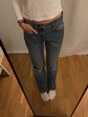 Blå raka jeans med slitning från Zara  - Säljer ett par blå raka jeans med hög midja och slitning vid knät. Jeansen har klassisk femficksdesign och är tillverkade i denim. Perfekta för en avslappnad och trendig look.