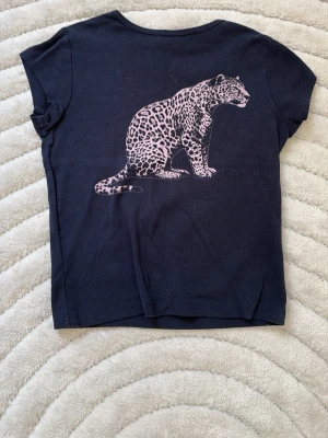 Marinblå subdued tröja - Cool marinblå T-shirt med ett stort leopardtryck på ryggen. T-shirten har korta ärmar och är rak i fram.