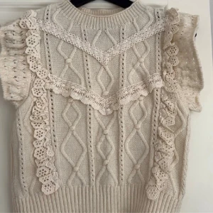 Vit stickad topp - Supersöt vit stickad topp från MNG med korta puffärmar och detaljerad spets längs axlar och bröst. Snyggt kabelstickat mönster och ribbad nederkant. Perfekt för dig som gillar romantisk och vintage-inspirerad stil.