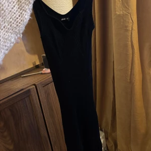 Svart ribbad långklänning Gina Tricot - Snygg svart långklänning från Gina Tricot med ribbad struktur och breda axelband. Klänningen har en djup v-ringning och är ärmlös, vilket ger en stilren och modern look. Perfekt för dig som gillar minimalistisk stil.