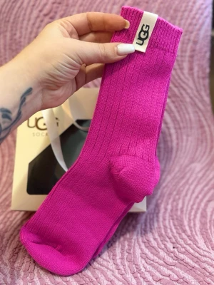 Rosa ribbade strumpor från UGG - Säljer ett par knallrosa ribbade strumpor från UGG med vit logotypetikett upptill. Strumporna är i mjukt och stretchigt material, perfekta för att ge en färgklick till din outfit. Klassisk modell med bekväm passform.