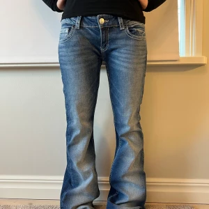 Blå bootcut jeans med broderade fickor, Gina Tricot.  - Säljer ett par blå bootcut jeans med snygga slitningar och kontrastsömmar från Gina Tricot. Jeansen har broderade bakfickor med lock och dekorativa knappar. Använda fåtal gånger. 