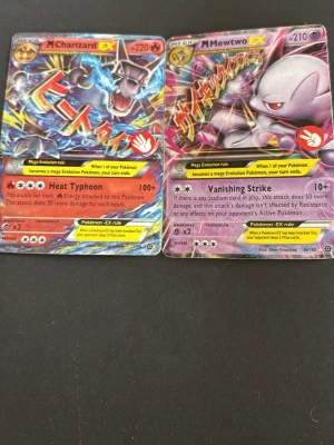 Pokémonkort Mega Charizard & Mewtwo EX - Två Pokémonkort: Mega Charizard EX och Mega Mewtwo EX. Båda korten har färgstarka illustrationer och holografisk yta. Text på engelska och japanska, med attackerna Heat Typhoon och Vanishing Strike. Perfekt för samlare eller Pokémonfans.