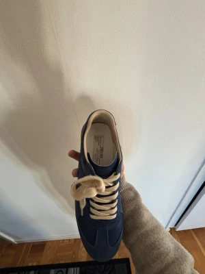 Marinblå sneakers från maison margiella - Snygga marinblå sneakers från maison margiella med beige snörning och klassisk gummisula i brunt. Ovandelen är i canvas och skon har en låg profil som passar till många olika stilar. Perfekt för dig som gillar enkel och tidlös design.