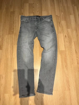 Grå raka jeans i klassisk modell - Säljer ett par grå jeans med rak passform och fem fickor. Jeansen har en klassisk look med knapp och dragkedja framtill samt subtila slitningar för en avslappnad vibe. Perfekta till vardagsstilen och funkar året runt.