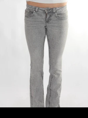 Grå bootcut jeans med fickdetaljer - Snygga grå jeans med bootcut passform och klassiska fem fickor. Jeansen har coola sömdetaljer och knappstängning fram. Perfekta för dig som gillar en avslappnad men trendig stil.