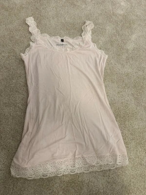 Ljusrosa spetskantad linnetopp Soulmate - Supersöt ljusrosa linnetopp från Soulmate med spetsdetaljer längs axelband, halsringning och nederkant. Mjuk och tunn kvalitet, perfekt för lager på lager eller som mysigt nattlinne. Romantisk vibe med fina spetskanter.