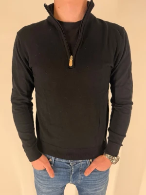 Svart Berto Lucci halvzip tröja - Snygg och stilren svart finstickad tröja med halvzip i storlek Small, från Berto Lucci milano. Tröjan har långa ärmar med ribbade muddar vid ärmslut och nederkant av tröjan. Perfekt för en stilren och fräsch look. Jag är ca 173 och väger 63kg. 