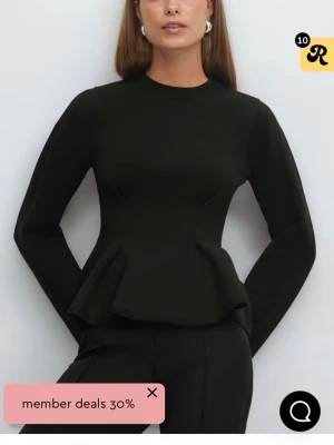 Svart peplum topp med lång ärm - Snygg svart peplum topp med lång ärm och rund hals. Toppen har en markerad midja och utsvängd nederdel som ger en feminin siluett. Perfekt att styla med både jeans och kostymbyxor för en trendig look.