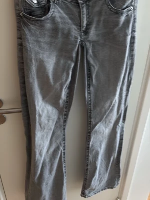 Gråa bootcut jeans - Säljer ett par gråa bootcut jeans med klassisk femficksdesign och normal midja. Jeansen har en lätt tvättad look och raka ben som går ut lite nedtill. Perfekta för dig som gillar en avslappnad men ändå trendig stil. Från Gina och har sytt ner dom själv.