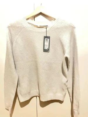 Vit stickad tröja från Vero Moda - Klassisk vit stickad tröja från Vero Moda med rund halsringning och långa ärmar. Tröjan har en enkel, rak passform och ribbade muddar vid ärmslut och nederkant. Perfekt basplagg för lager på lager och enkel att matcha.