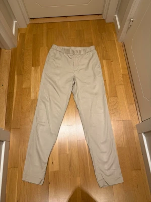 Beige chinos från These Glory Days - Snygga beige chinos från These Glory Days i rak passform. Tillverkade i ett mjukt och slitstarkt tyg som känns skönt mot huden. Klassisk design med knapp och dragkedja framtill, perfekta för en clean och stilren look.                                                                          Modellen är 185cm lång och väger 82kg.