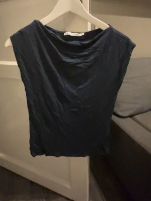 Mörkblå topp från 157 - En enkel och stilren mörkblå topp från 157 i storlek XS. Toppen har en lös passform och är ärmlös, vilket gör den perfekt för varmare dagar. Tillverkad i mjukt material som känns skönt mot huden. Snygg att matcha med både jeans och kjol.