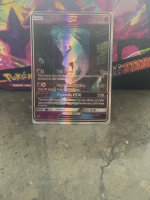 Mewtwo GX Pokémonkort holografiskt - Säljer ett holografiskt Mewtwo GX-kort från Pokémon Trading Card Game. Kortet har en futuristisk design med Mewtwo i ett laboratorium, HP 190 och attacker som Full Burst, Super Absorption och Psystrike GX. Kortet har en skimrande yta och är tryckt på tjockt papper.