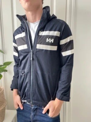 Helly Hansen vindjacka - Helly Hansen vindjacka, inga defekter. Storlek 14 vilket motsvarar i helly Hansen storlekar S i vanlig. Helly Hansen brukar vara större i storleken. Modellen som bär den är 180 cm 75 kg och jackan är för liten på honom. Kom med frågor! 