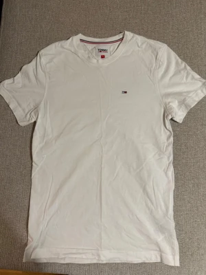 Vit t-shirt från Tommy Jeans - Klassisk vit t-shirt från Tommy Jeans med liten broderad logga på bröstet. T-shirten har rund halsringning och korta ärmar. Tillverkad i mjuk bomull för en skön och enkel stil.