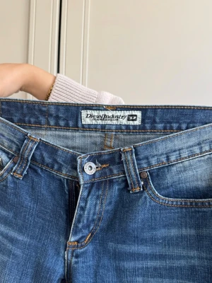 Blå bootcut jeans från Diesel - Säljer ett par as snygga blå bootcut vintage jeans från Diesel. De är perfekt låga i midjan och sitter åt runt rumpan men är utsvängda annars. Extremt snygga på alla! 