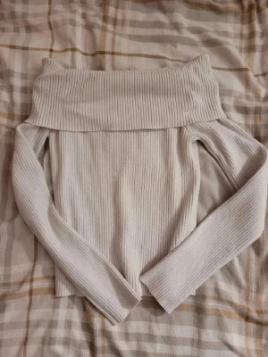 Off shoulder ribbad tröja vit - Trendig off shoulder tröja i ribbat material och vit färg. Långa ärmar och bred krage som viks ner över axlarna. Perfekt för dig som vill ha en stilren och modern look.