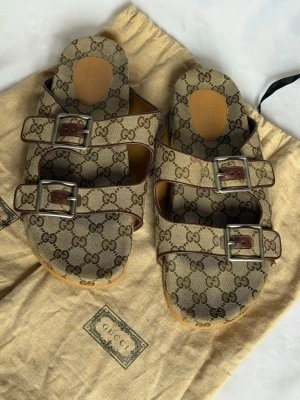 Äkta Gucci sandaler - Äkta Gucci sandaler  (SLUTSÅLDA)  Storlek 11  (se bild för mått)  Väldigt fint skick, inget att anmärka på. Levereras med skopåsarna