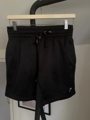 Svarta träningsshorts från Gymshark - Svarta shorts från Gymshark med elastisk midja och snörning. Perfekta för träning, tillverkade i ett mjukt och lätt polyestermaterial. Klassisk design med liten logga på benet och normal passform. Shortsen är som nya eftersom att de bara är använda en gång, hör av dig vid minsta fundering och pris kan diskuteras! 🤩🙌