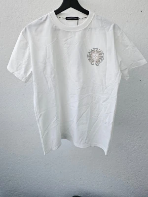 Vit t-shirt från Chrome Hearts - Snygg vit t-shirt från Chrome Hearts med ett litet tryck på bröstet. Klassisk rund hals och korta ärmar. Perfekt till jeans eller shorts för en clean och stilren look.