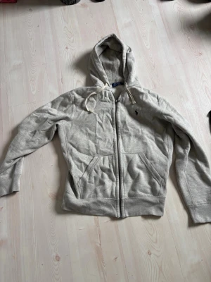 Grå ziptröja från Polo Ralph Lauren - Grå ziptröja från Polo Ralph Lauren, den är andvönda några gånger men jag har växt ut den och nu har den bara legat och inte kommit till andvändning.. bredd 86cm, längd 98cm