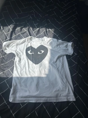 Comme des Garçons PLAY T-shirt – Vit – Storlek L – Helt ny - Säljer en äkta Comme des Garçons PLAY T-shirt i vitt med den klassiska svarta hjärtloggan. Tröjan är i helt nytt skick och storlek L. Perfekt för dig som vill ha en stilren designer-T-shirt som passar till allt.  Detaljer: • Märke: Comme des Garçons PLAY • Färg: Vit med svart hjärtlogga • Storlek: L • Skick: Helt ny • Material: 100% bomull • Unisex-modell • Original etiketter finns kvar på tröjan  Skicka gärna meddelande vid frågor eller om du vill ha fler bilder!