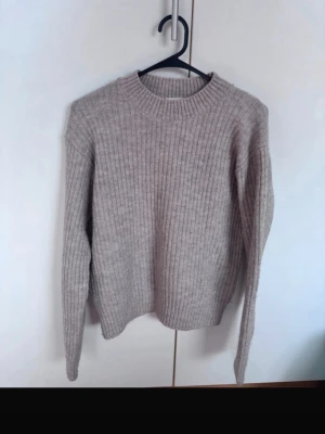 Beige ribbstickad tröja - Mysig beige ribbstickad tröja med rund halsringning och långa ärmar. Tröjan har en enkel och stilren design som passar perfekt till jeans eller kjol. Materialet ser ut att vara mjukt och skönt, perfekt för kyligare dagar.