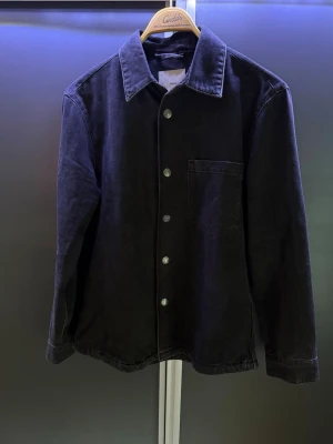 Svart overshirt Mango - Stilren svart overshirt från MNG med klassisk krage, knappstängning framtill och en bröstficka. Perfekt skick då jag knappt använd den. Passar en M eller stor S. Skriv vid andra frågor!